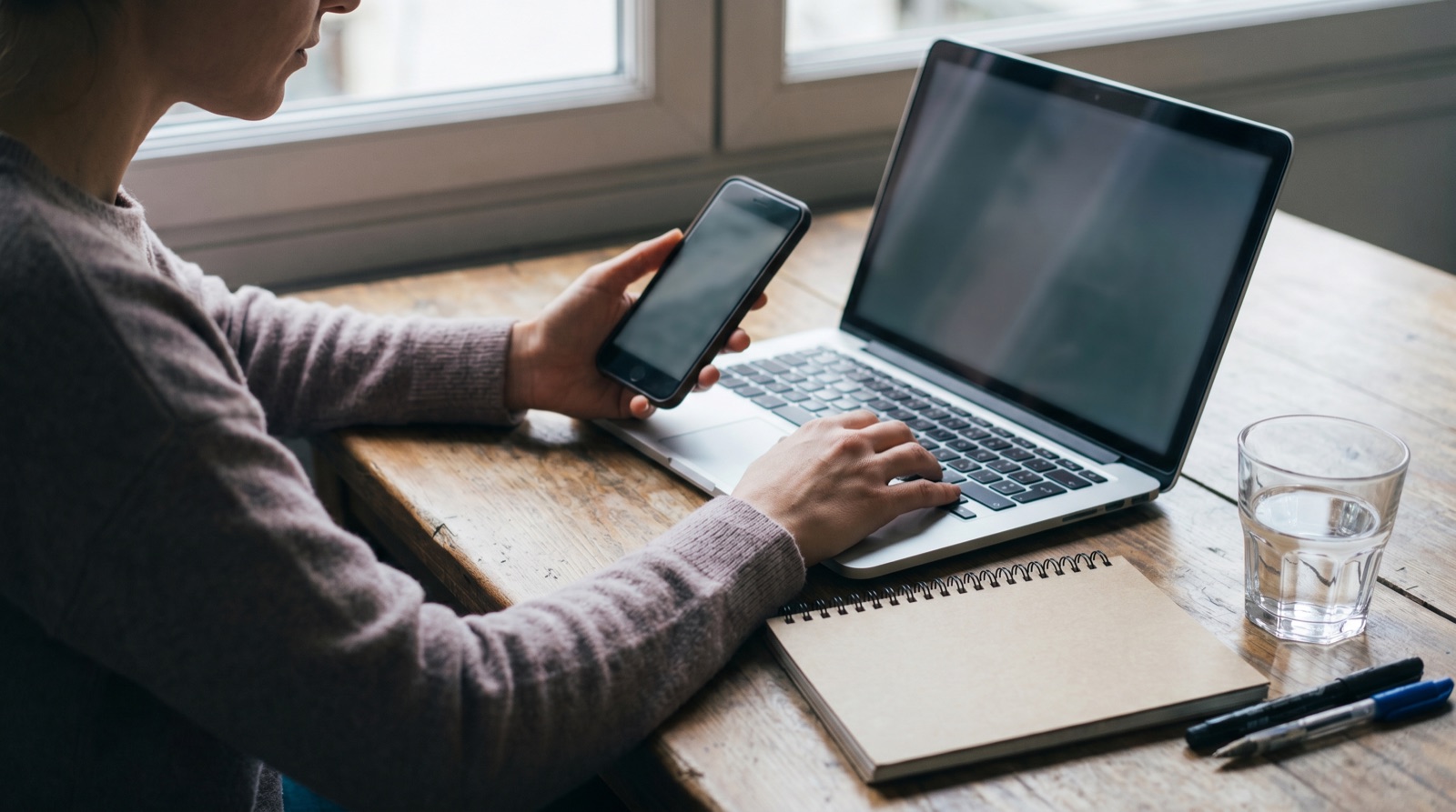 A person comparing results on their phone and laptop at a desk, weighing SEO against GEO
