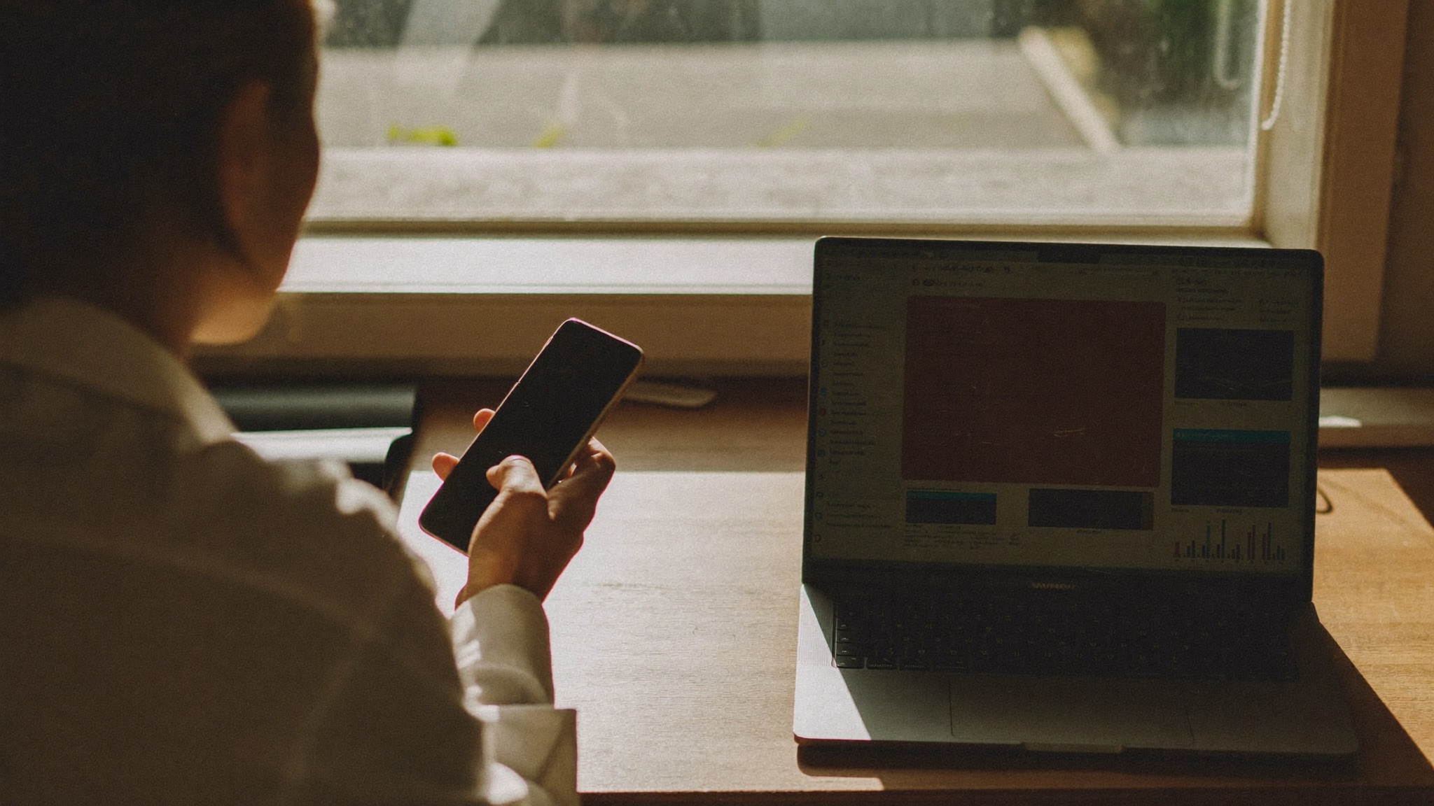 A small business owner comparing ad results on a laptop and phone at a desk