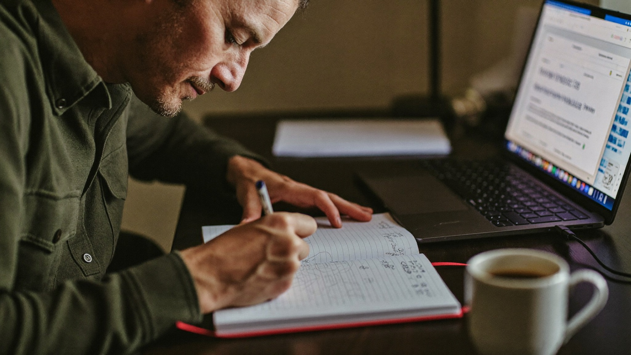 A small business owner reviewing ad campaign numbers on a laptop at a workshop desk, coffee beside the keyboard